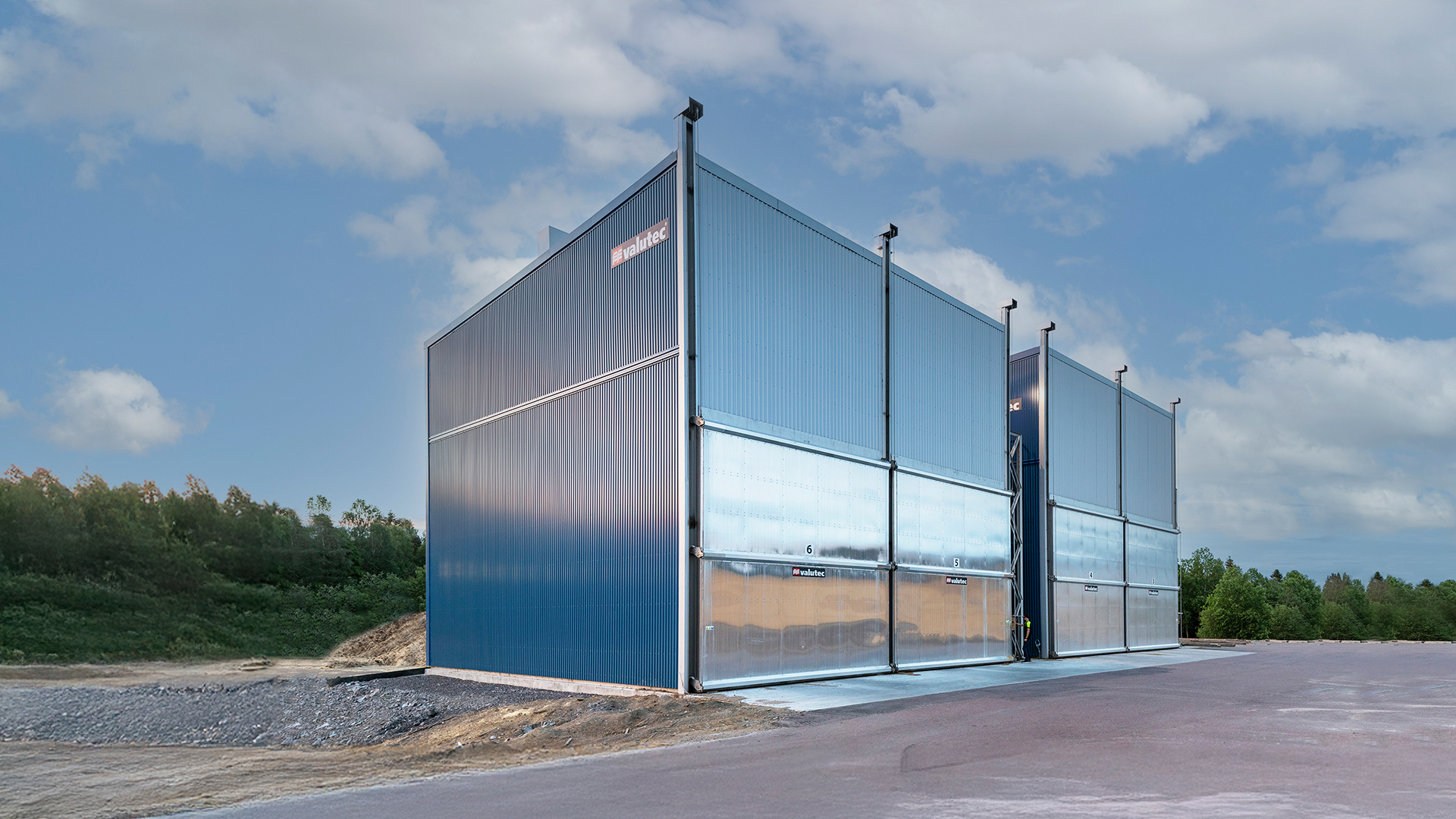 Valutec kammartorkar i metall med blå fasad och stora portar, placerade på sågverksområde.