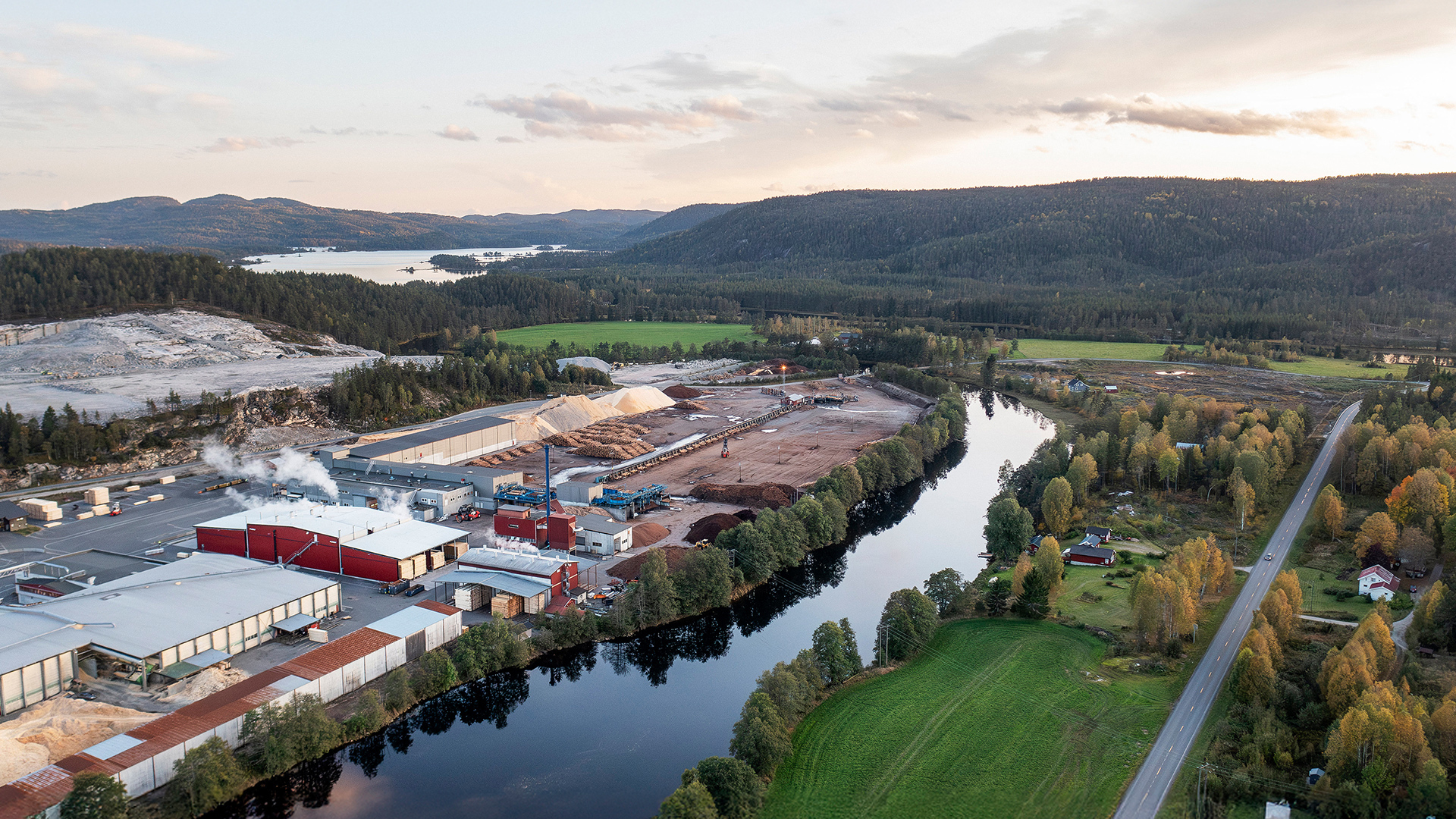 Flygbild över sågverk och virkestorkar från Valutec, omgivet av skog, vatten och landskap.