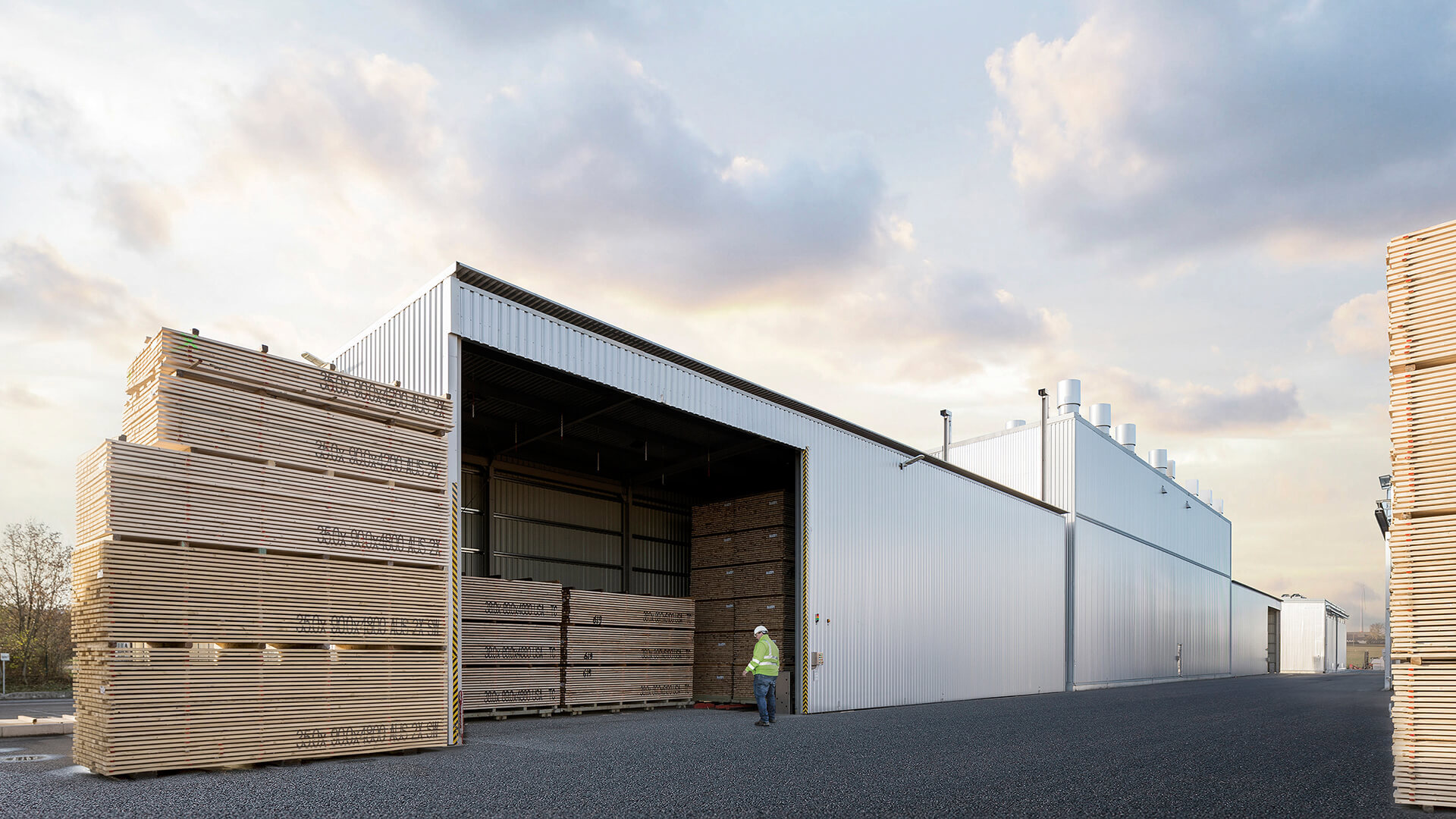 Person i skyddshjälm framför staplat virke vid en kanaltork.