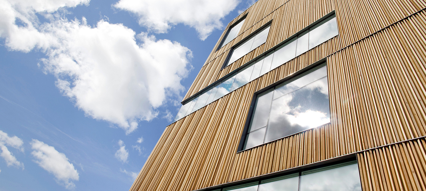 Moderna trähusfasader med stora fönster som speglar himlen.