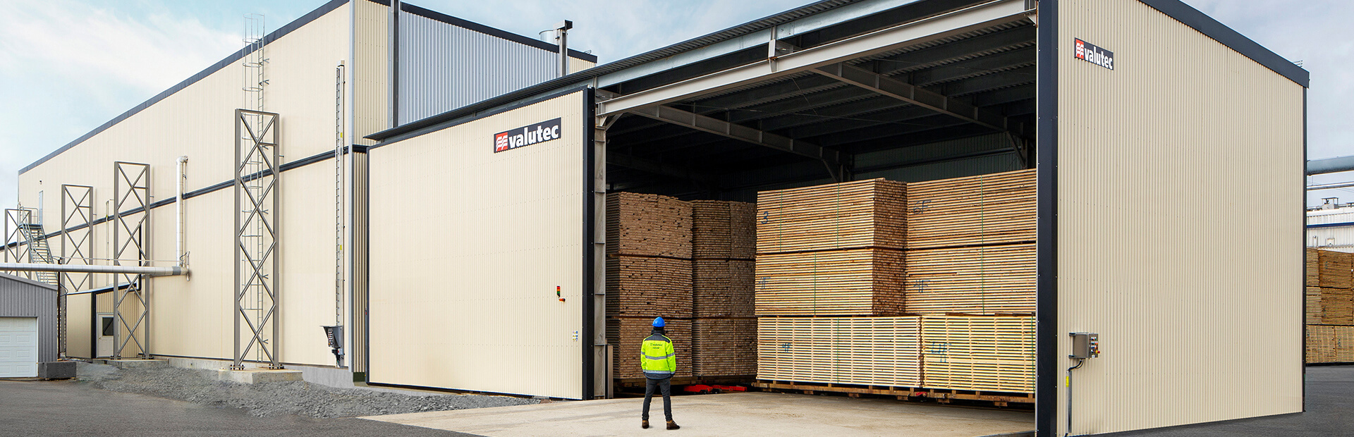 Valutec kanaltork TC med öppnad port, fylld med staplade virkespaket redo för torkning. En person i skyddsutrustning står framför anläggningen.