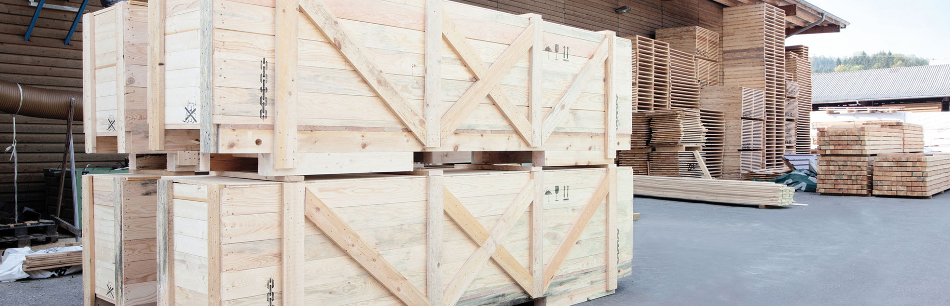 Virkespaket och träemballage staplade utanför en Valutec OTC-kanaltork, med mer virke synligt i bakgrunden.