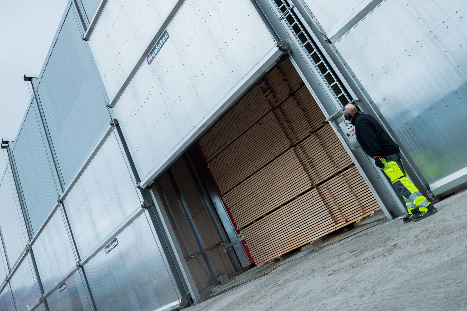 Arbetare utomhus tittar på en port som öppnas med virke innanför.