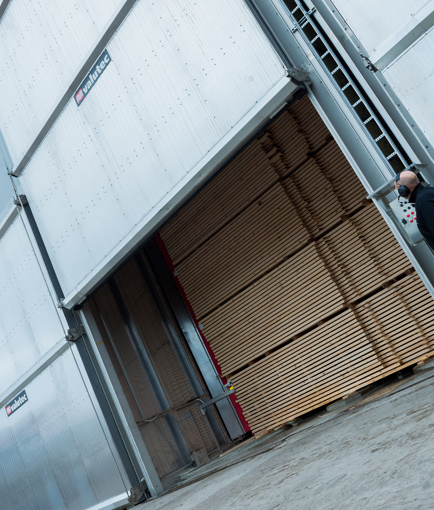 Arbetare utomhus tittar på en port som öppnas med virke innanför.