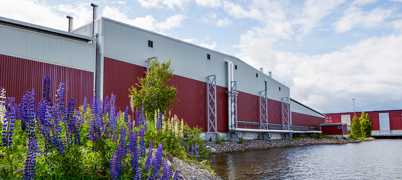 Valutecs röda virkestorkar vid vattnet, med blommor i förgrunden – exempel på hållbarhet och miljöhänsyn.