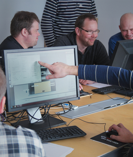 Fyra personer sitter vid datorer i ett möte, en pekar på datorskärmen.