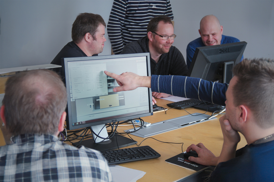 Fyra personer sitter vid datorer i ett möte, en pekar på datorskärmen.