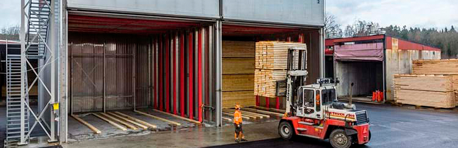 Truckmatad kammartork från Valutec, med en truck som lastar in virke. En operatör i orange arbetskläder står bredvid.