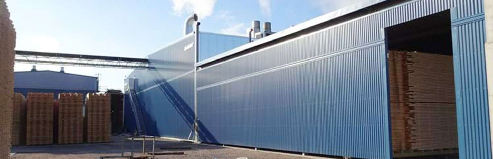 Blå kanaltork FB från Valutec, med staplat virke synligt vid ingången till anläggningen.