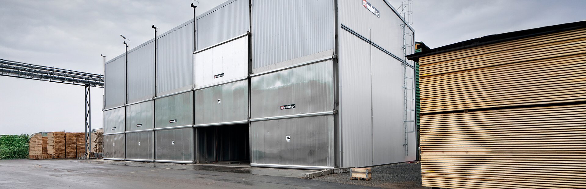 Valutec truckmatad kammartork i plåtfasad med öppna portar, staplat virke vid sidan.